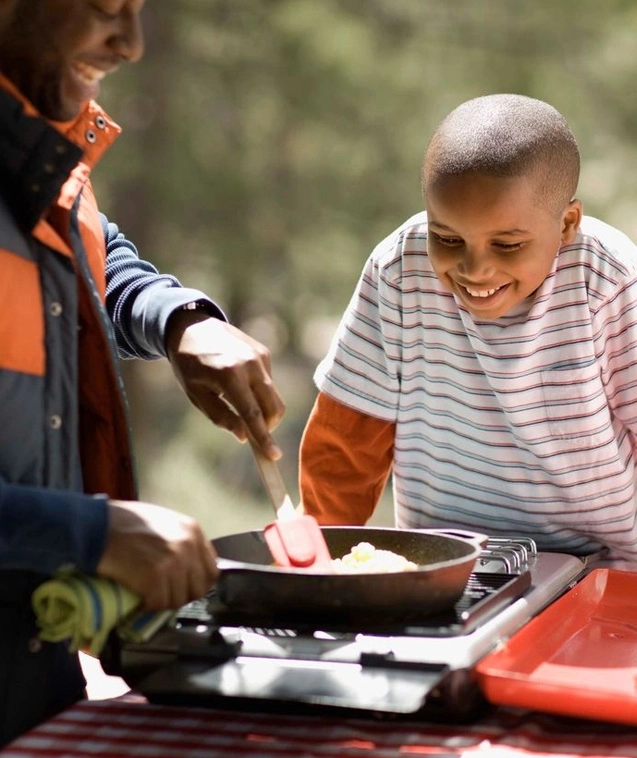 A man and boy cooking food on an outdoor grill.