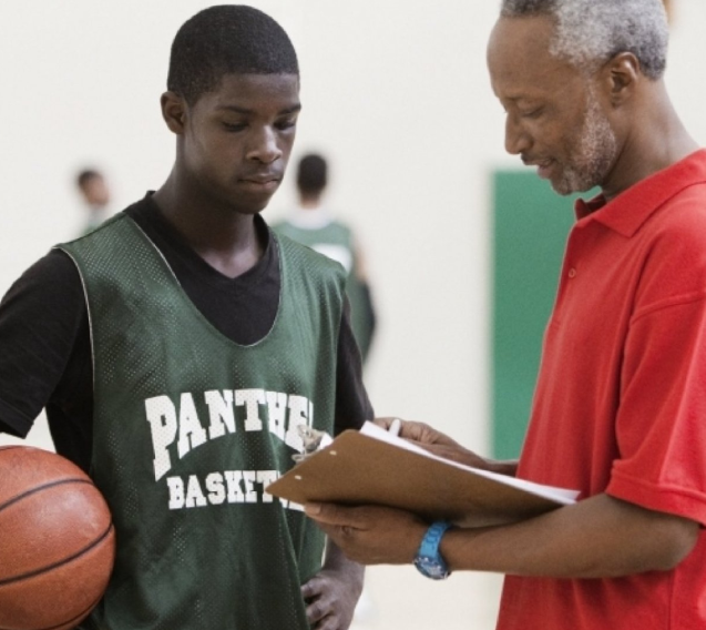 A man is talking to another man in a basketball uniform.