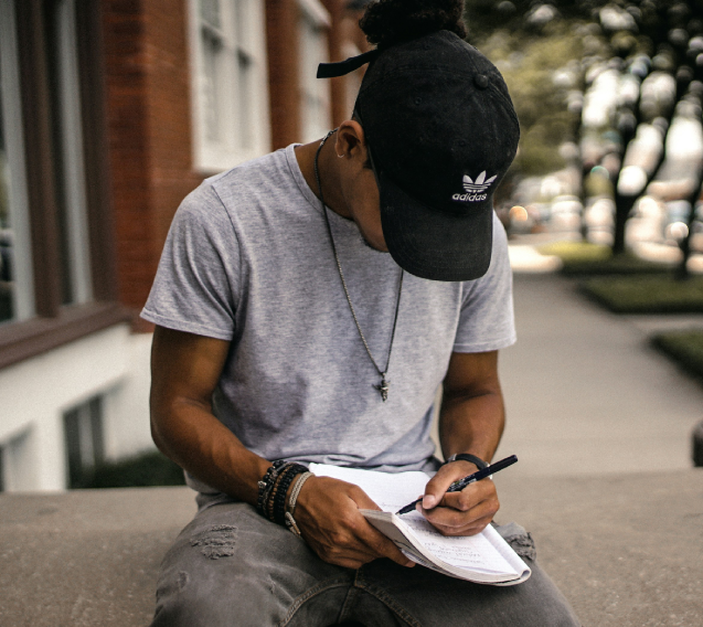 A man sitting on the ground writing in his notebook.